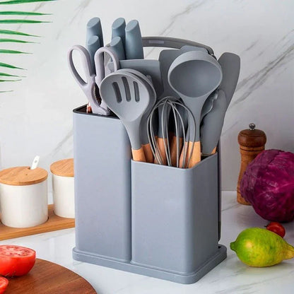 Organizador gris con utensilios de cocina de silicona y mango de madera sobre encimera con verduras y especieros